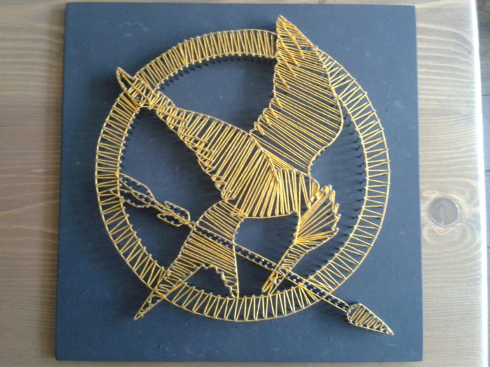 eine Abbildung vom Logo des Films Tribute von Panem, gelbes String Art Bild