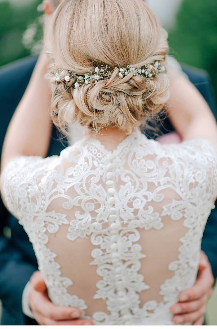 Brautkleid mit Spitzenelementen, Hochsteckfrisur mit kleinen weißen Blumen, blonde Haare