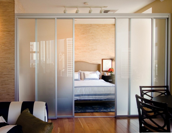 Raumtrennung mit Schiebetüren aus Glas, ein großes Bett, gestreiftem Sofa und Eszimmerstühle