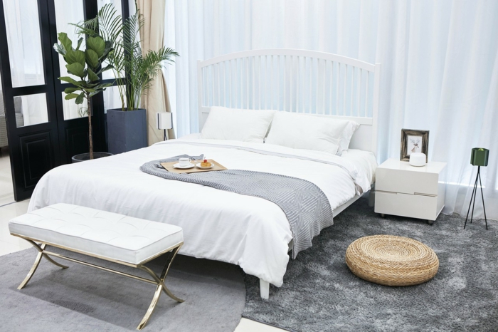 graue Teppiche, ein weißes Bett mit zwei Kissen, zwei Pflanzen in der Ecke, moderne Zimmer