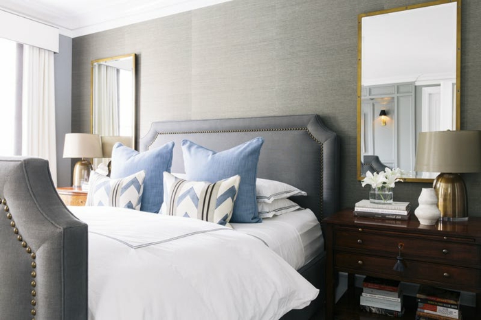 ein Bett in grauer Farbe mit blauen Kissen, zwei Spiegel und zwei Regale, zwei Lampen