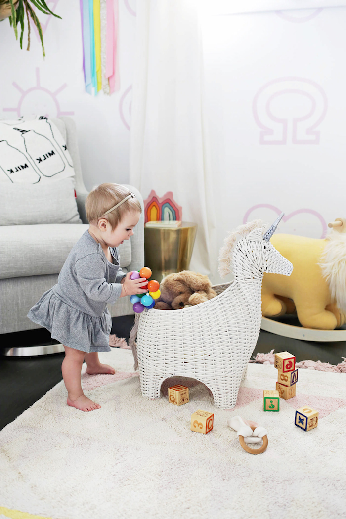 Babyzimmer Einrichtung, süßes Baby mit grauem Kleid, Kuscheltiere und Spielzeuge aus Holz, Einhorn aus Rattan