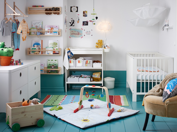 Babyzimmer Einrichtung, weiße Wandfarbe und blauer Boden, viele Spielzeuge, Kinderbücher und Babykleider