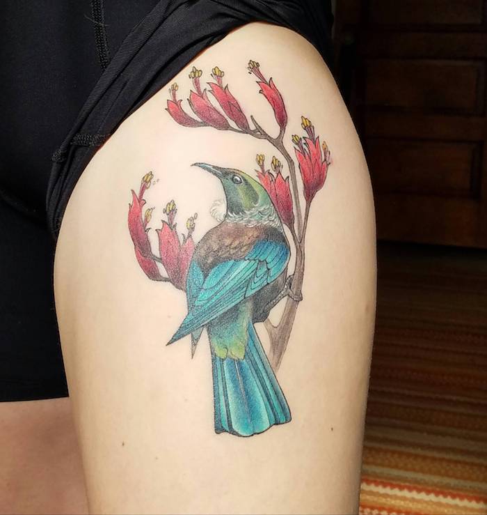 frau mit farbigem bein tattoo, vogel in blau und braun, vogel am zweig, rote blüten