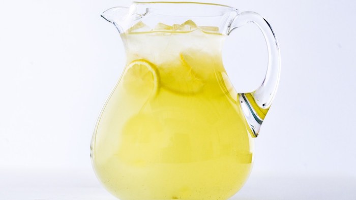 ein großer krug mit einer gelben hausgemachten limonade mit eis und mit vielen kleinen gelben zitronen, eine amerikanische limonade selber machen