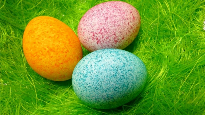 drei Eier in gelber, roter und blauer Farbe, Ostereier färben, Effekte mithilfe von Reis erzeugen