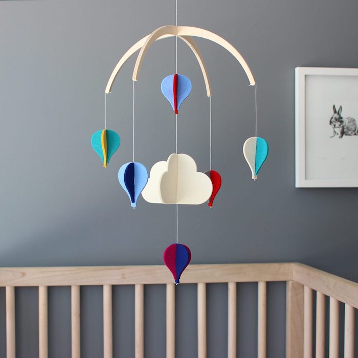 Mobile fürs Babyzimmer in Form von Wolken und Heißluftballons aus Filz, Wandfarbe Grau, Babybett aus Holz 