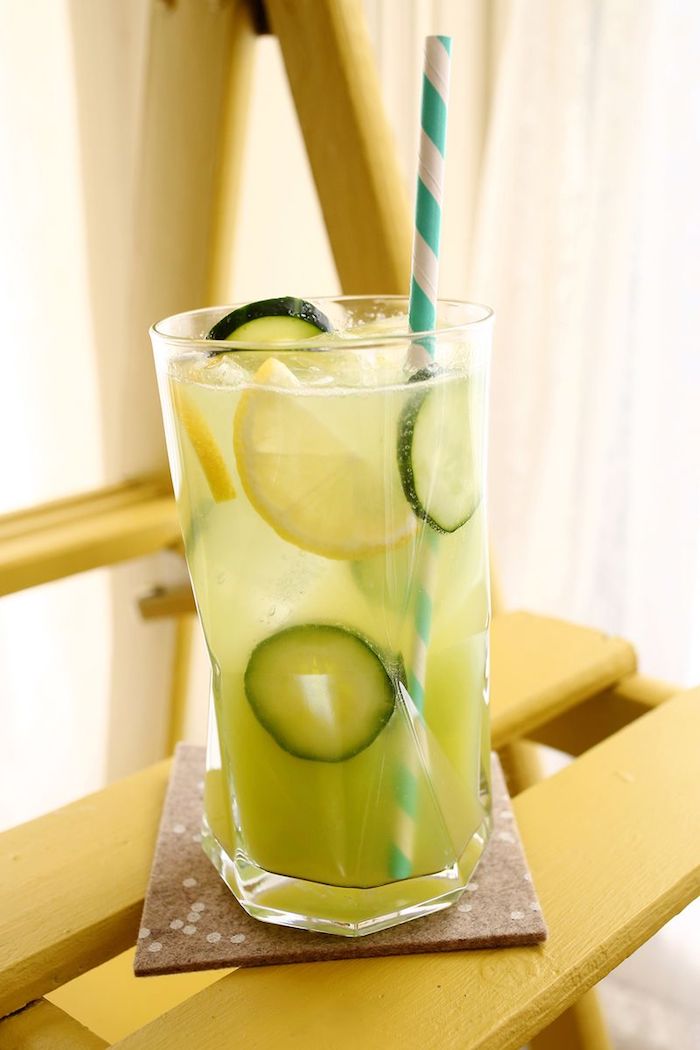 ein glas mit einer erfrischungsgetränk mit vielen kleinen grünen gurken und gelben zitronen und mit einem blauen strohhalm, eine hausgemachte limonade