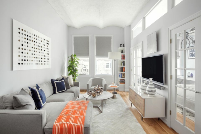 ein graues Sofa, blaue Kissen, orange Decke Fernsehwand, kleines Zimmer einrichten