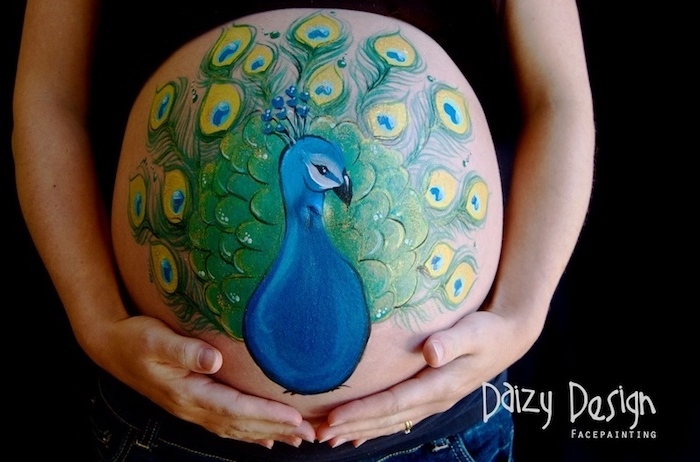 bild mit einem großen blauen pfau mit grünen federn, eine schwangere frau mit einem bemalten bauch, babybaauch bemalen motive