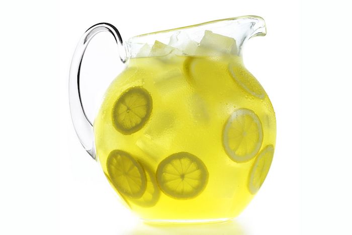 großer krug aus glas, eine hausgemachte limonade mit vielen kleinen gelben zitronen und mit eis