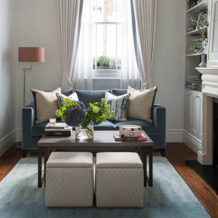 eine blaue Couch, symmetrisch gelegte Kissen, zwei Hocker, kleines Wohnzimmer einrichten