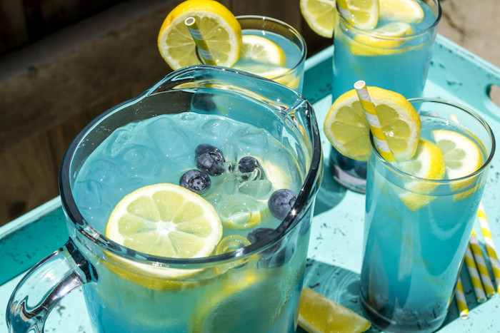 drei kleine blaue gläser mit einer blauen limonade mit eis, vielen gelben zitronen und mit drei gelben strohhalmen, eine hausgemachte limonade