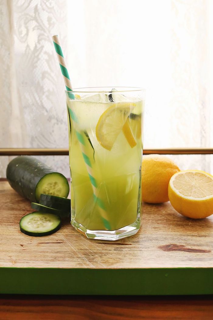 ein fenster und ein schneidebrett, ein glas mit einer grünen limonade mit grünen gurken, eis und mit vielen gelben zitronen, eine limonade selber machen