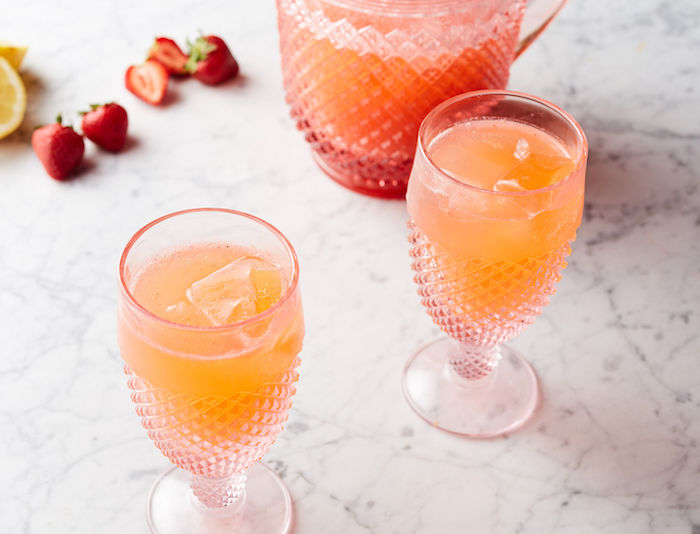 ein krug mit einer hausgemachten limonade mit eis, ein tisch und rote erdbeeren und gelbe zitronen, orangen limonade selber machen