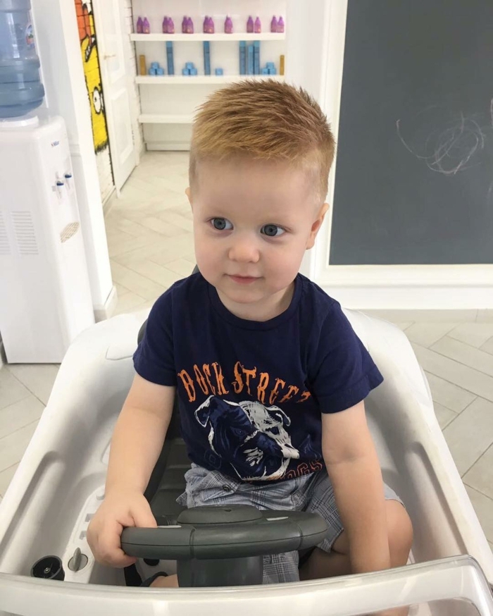 rothaariges Kleinkind in einem Spielauto, seitlich rasiert, längeres Haar am Oberkopf