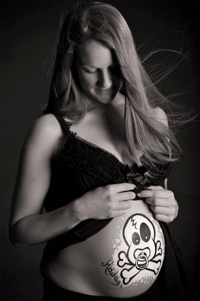 ein weißer totoenkopf mit schwarzen augen und einem schnuller, babybauch shooting ideen, eine junge schwangere frau mit einem großen bemalten babybauch