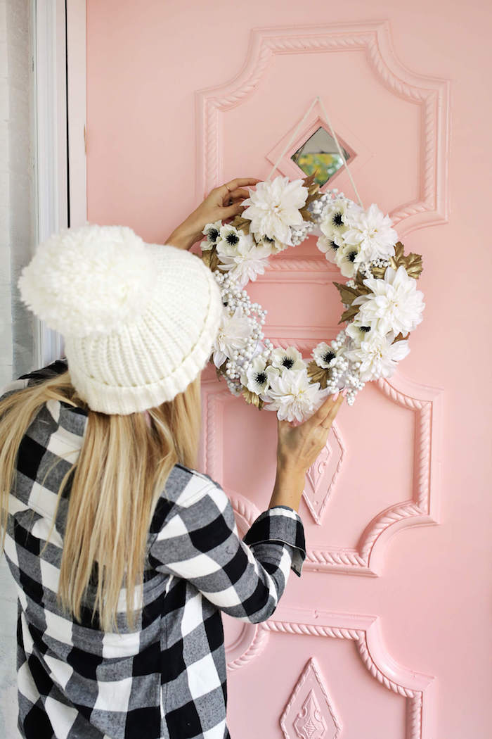 Blumenkranz aufhängen, Frühlingsdeko für die Haustür, Frau mit kariertem Hemd und weißer Mütze