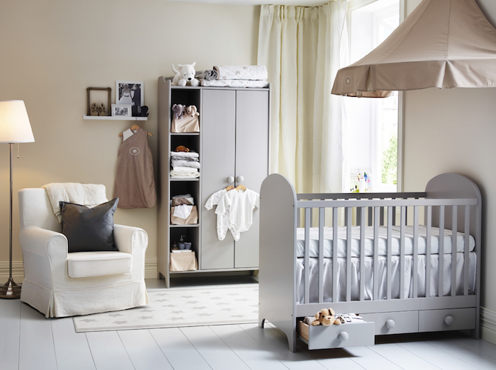 Babyzimmer in Pastellfarben, graues Babybett mit Schubladen, weißer Sessel, Babykleider und Kuscheltiere