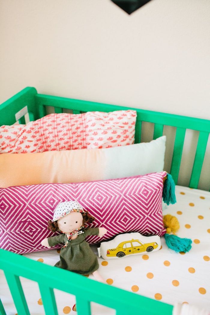 Grünes Babybett aus Holz, bunte Kissen, Puppe mit Mütze, Bettwäsche mit gelben Dots