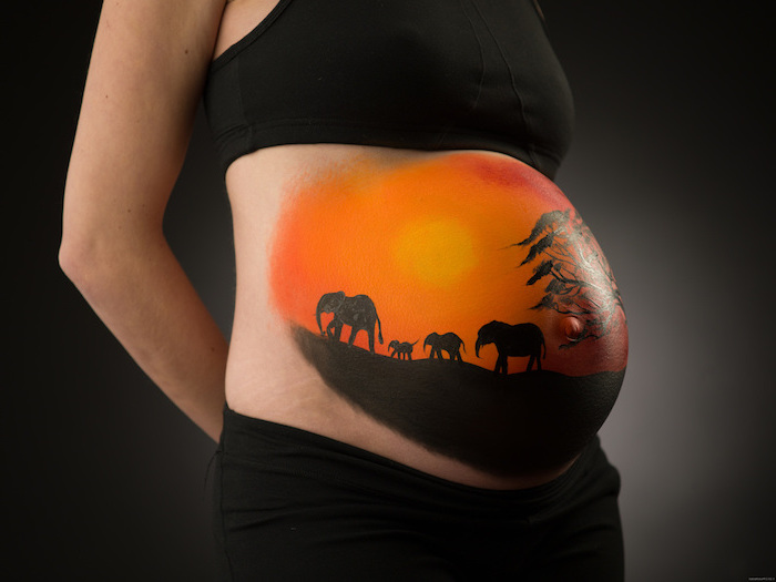 sonnenuntergang, vier schwarze elefanten und ein großer schwarzer baum, eine schwangere frau mit einem bemalten großen babybauch
