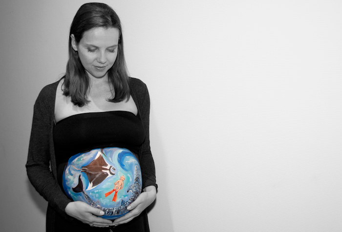 ein bild mit meer, blauen wellen, hai und einem schwimmenden jungen, eine schwangere frau mit einem großen bemalten babybauch