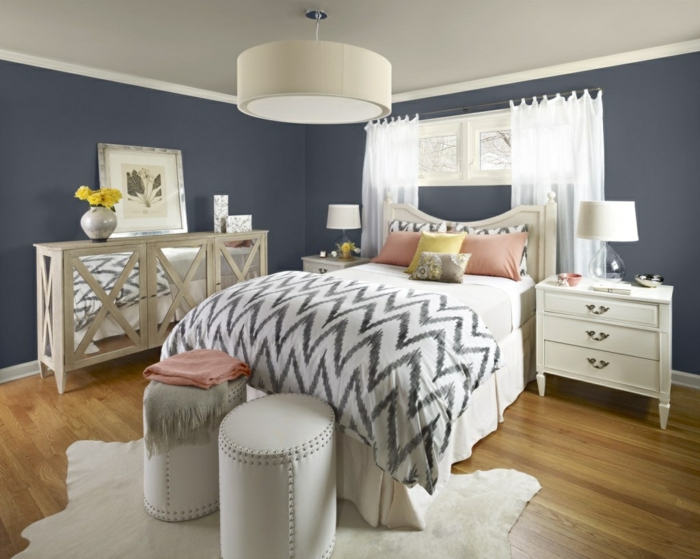zwei weiße Hocker, Wandfarbe Hellgrau, bemusterte Bettdecke und Kissen