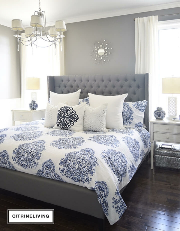 weiße Decke, blaue Motive, gepolstertes Bett, ein Spiegel mit silbernem Rahmen