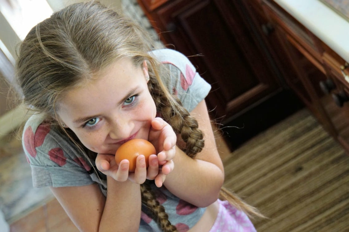 ein niedliche Mädchen trägt ein oranges Ei, Eier bemalen mit Kindern