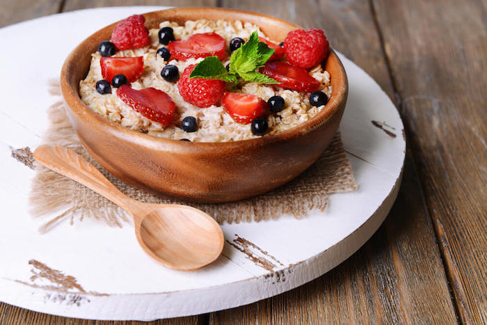 porridge rezept kalorienarm, eien hölzerne schüssel, löffel, frühstück mit obst, geschnittene erdbeeren