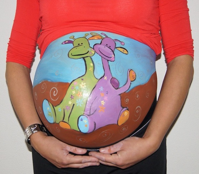 blauer himmel, zwei grüne und violette giraffen, eine schwangere frau mit einem großen bemalten babybauch, eine hand mit einem uhr