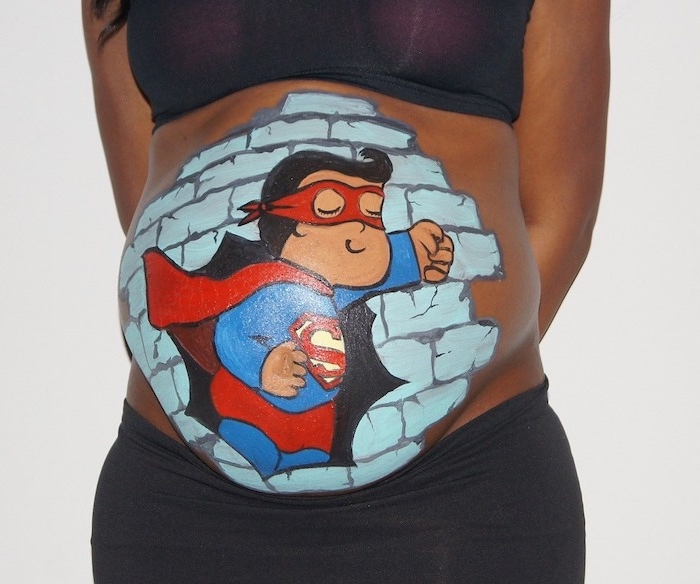 schwarze haare, ein bild mit einer blauen wand und einem fliegenden superman, eine schwangere frau mit einem großen bemalten babybauch