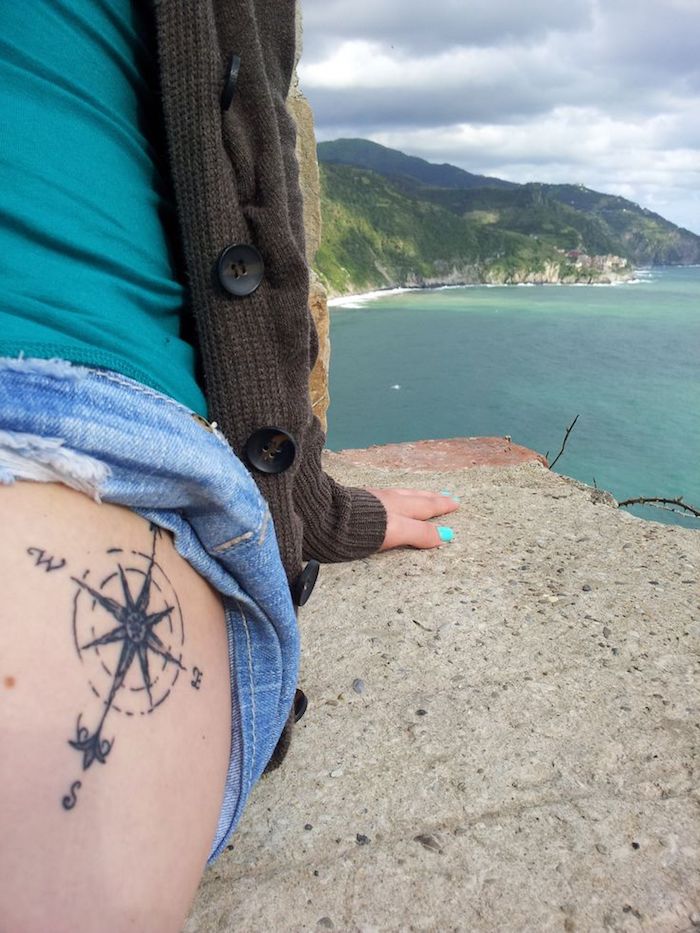 tattoo oberschenkel,kurze hellblaue jeans, kompass in schwarz und grau, grüne bluse, weste