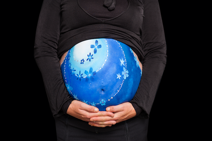 eine schwangere frau mit einem blauen babybauch mit vielen kleinen und großen blumen, babybauch bemalen lassen