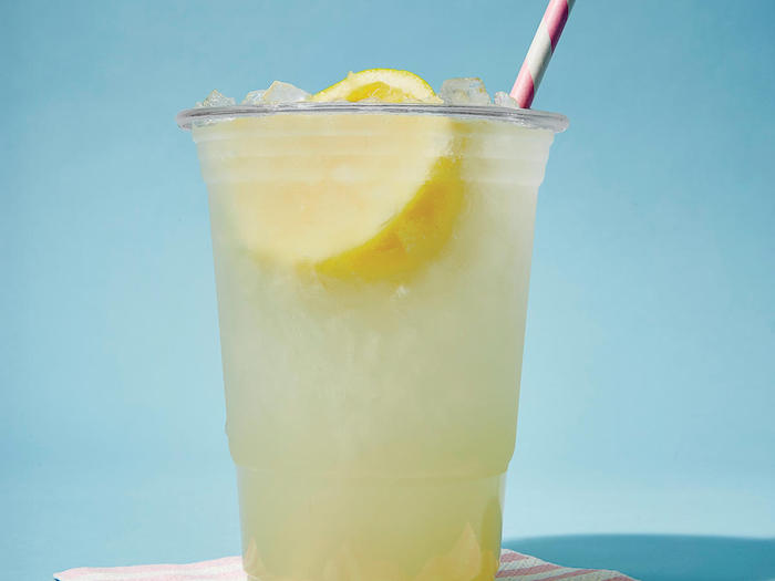 ein glas mit einer hausgemachten gelben limonade mit eis und mit einer gelben zitrone und mit einem roten strohhalm 