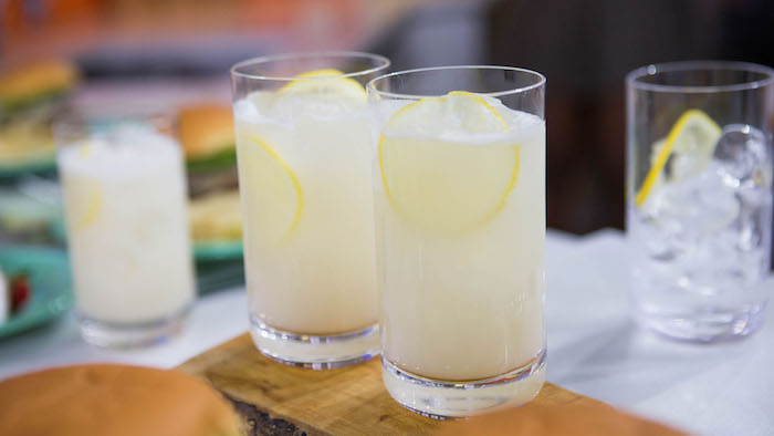 ein holzbrett und zwei gläser mit einer gelben selbstgemachten limonade mit zitronen und eis
