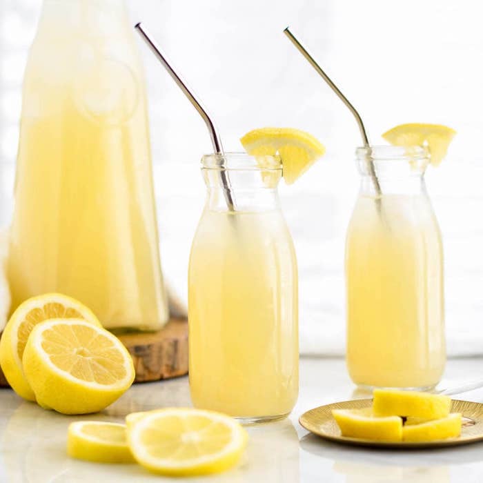 zwei große gläser mit einer selbstgemachten limonade mit eis und mit vielen gelben zitronen, ein holzbrett und ein großer krug mit einer gelben zitronnenlimonade