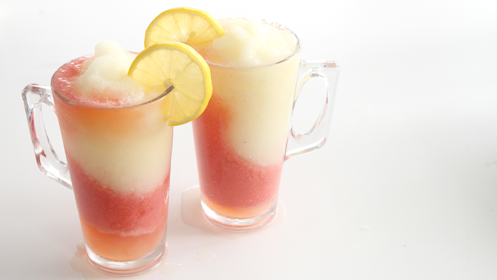 zwei gläser mit einer pinken limonade mit zwei kleinen gelben zitronen, eine zitronenlimo selber machen, orangen limonade selber machen