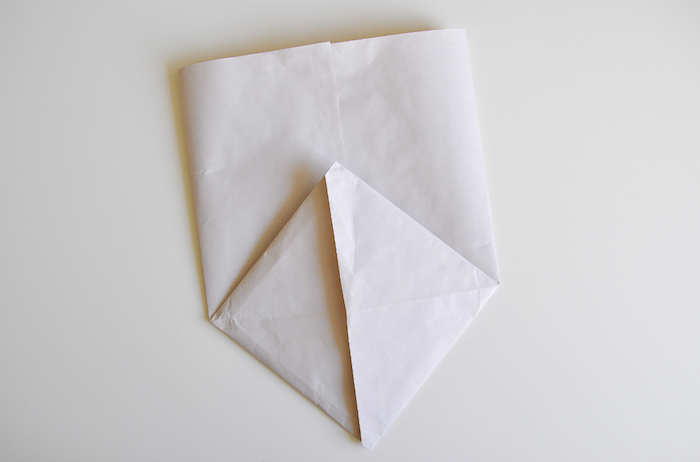eine kleine weiße gefaltete tüte aus papier, basteln mit papier, ein weißer tisch und eine gefaltete papiertüte