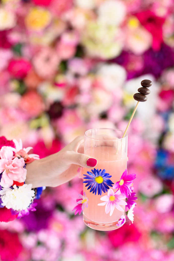 Cocktail in Glas mit bunten Blumen, Armband aus Blüten, roter Nagellack