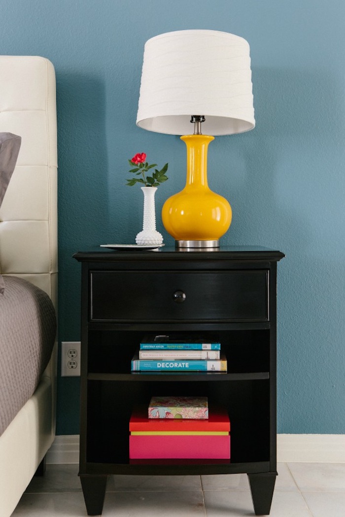 schlafzimmer Einrichtung, Wandfarbe Himmelblau, schwarzer Nachttisch aus Holz, Nachttischlampe mit weißem Schirm, kleine Vase, rote Rose