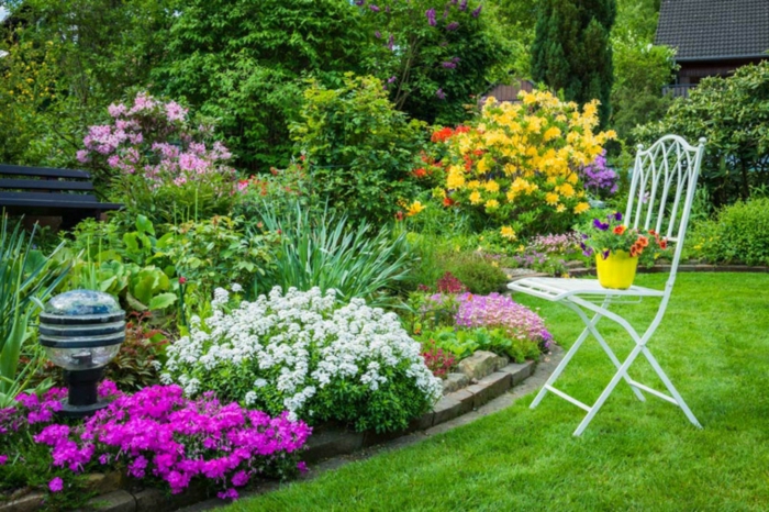 bunte Beete, ein weißer Stuhl als Dekoration, gepflegter Rasen, Garten gestalten mit wenig Geld