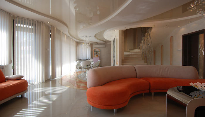 ein oranges sofa und ein wohnzimmer mit fenstern und weißen wänden, ein tisc und kleine weiße stühle, eine große weiße treppe und kleine gelbe lampen, zimmer einrichten ideen