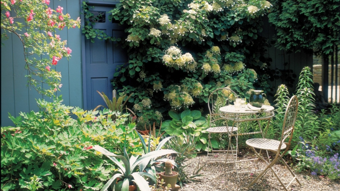 weiße, gelbe und rosa Blumen, Ziersträuche, kleine Gartenmöbel, Kies Bodenbeleg, günstige Gestaltungsideen Garten