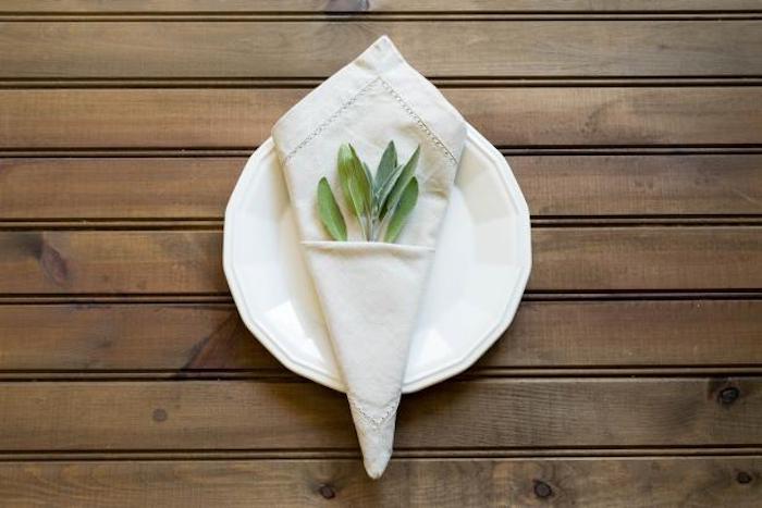 ein weißer teller mit einer weißen serviette mit grünen pflanzen, ein tisch aus holz, bestecktaschen anleitung
