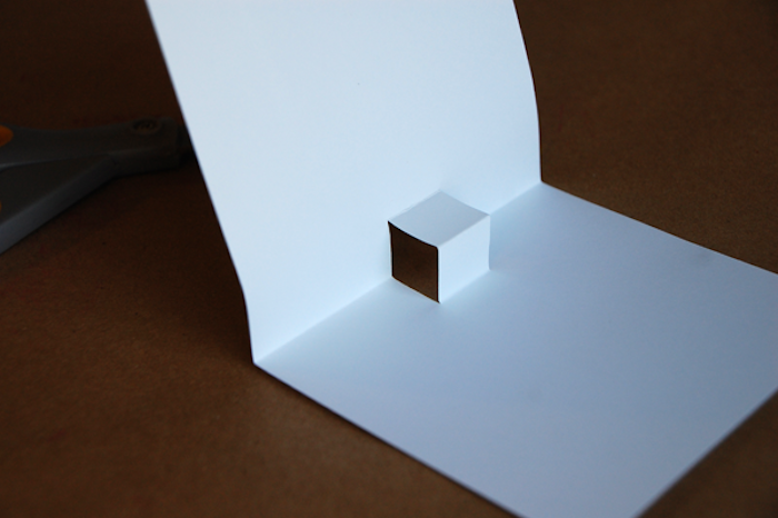 tisch aus holz und eine kleine weiße selbstgebastelte pop up karte aus papier, pop up karten selber machen, basteln mit papier