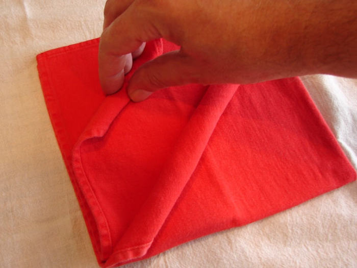 eine weiße decke und eine kleine rote gefaltete serviette und eine hand, servietten falten einfach und wirkungsvoll