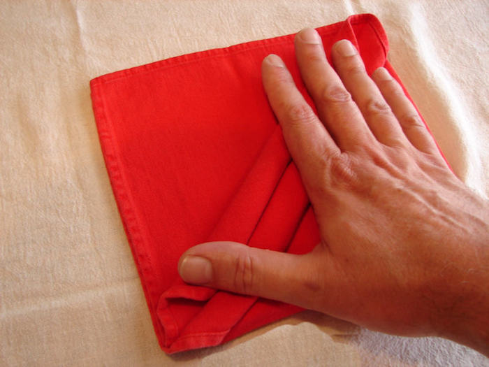 eine weiße decke und eine kleine rote gefaltete serviette und eine hand, servietten falten anleitung, eine bestecktasche falten