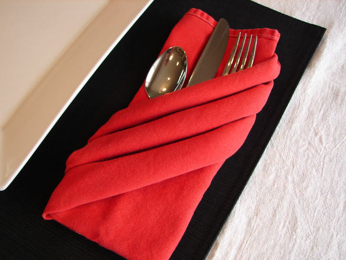 servietten falten hochzeit, ein tisch aus holz und eine rote gefaltete bestecktasche mit einem messer, einem löffel und einer gabel, bestecktaschen falten