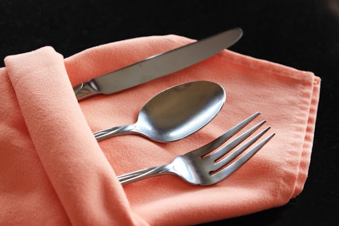 tischdekoration selber basteln, eine orange gefaltete bestecktasche mit einem messer, einem löffel und einer gabel, servietten falten hochzeit 
